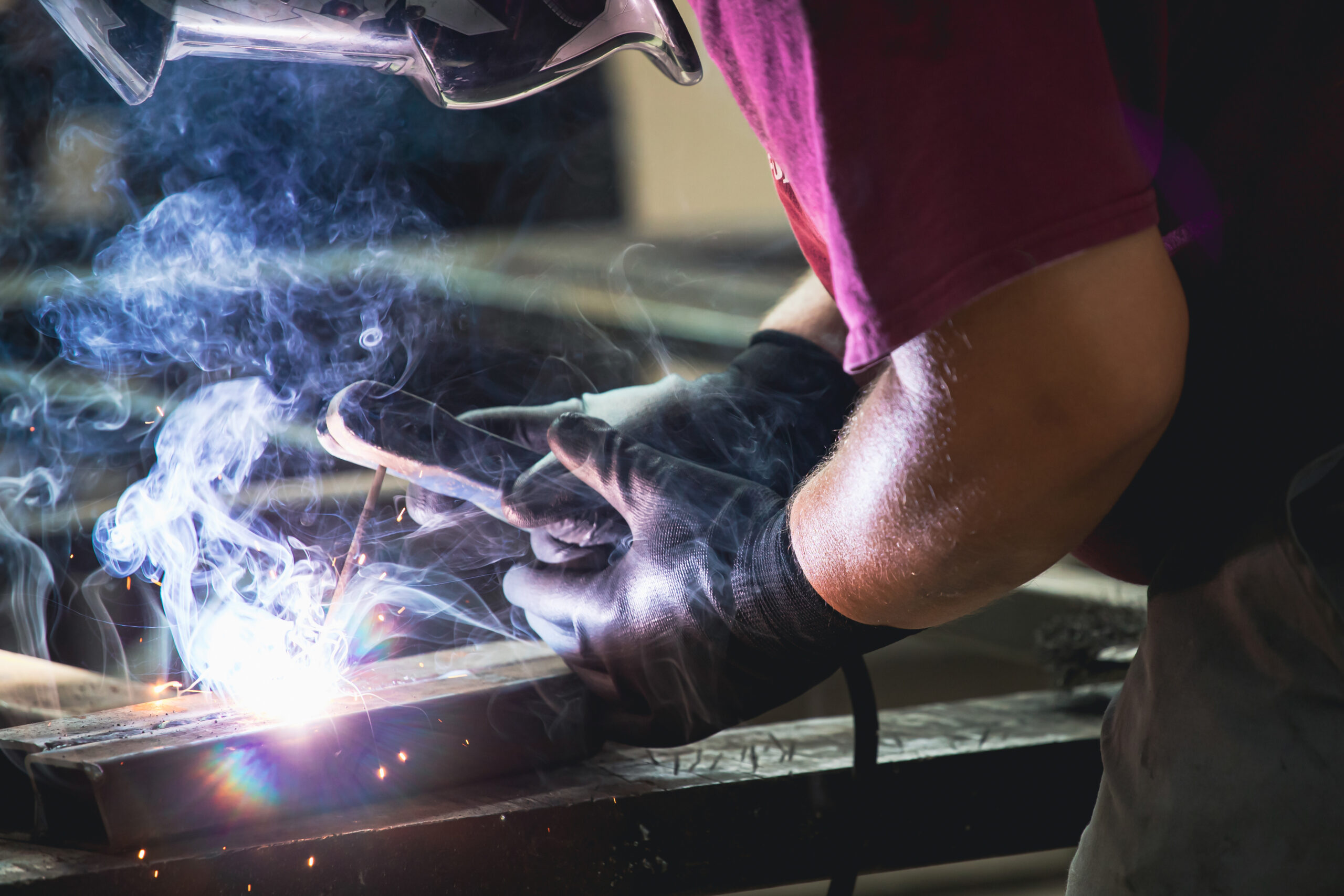 Handyman performing welding and grinding at his workplace in the workshop, while the sparks "fly" all around him. He is wearing a protective helmet and equipment.