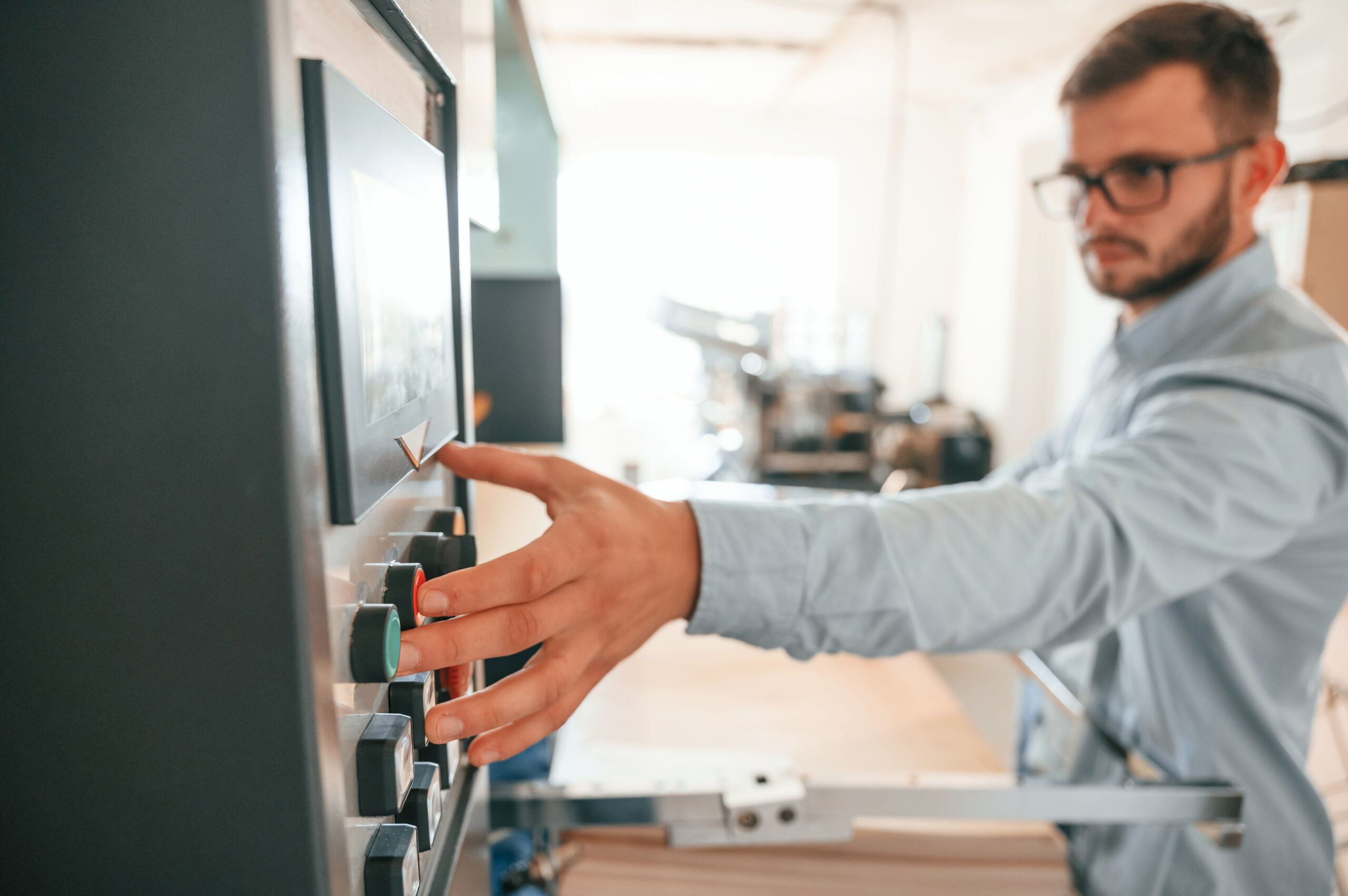 Pressing the knobs on the machine. Print house worker in white clothes is indoors.